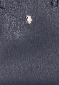 Sac fourre-tout en cuir bleu marine avec texture granuleuse et un petit logo argenté de cavalier sur le devant. Dispose de deux poignées supérieures pour le transport.