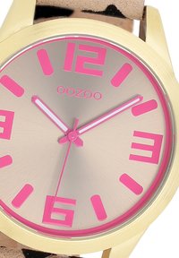 Montre dorée avec un cadran métallique rose, des index horaires roses audacieux et deux aiguilles blanches. Bracelet en cuir avec un motif tacheté.