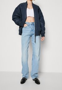 Chaqueta de bombardero azul marino sobre un top corto blanco, combinada con jeans rectos de un azul claro y zapatos negros con acentos de hardware plateado.