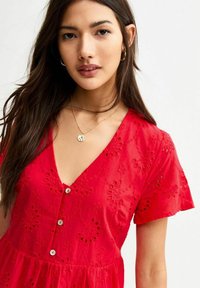 Rotes Kleid mit V-Ausschnitt, dekorativer floralem Stickerei, kurzen Ärmeln und Knopfdetails an der Vorderseite. Glatte Textur, leichtes Material.