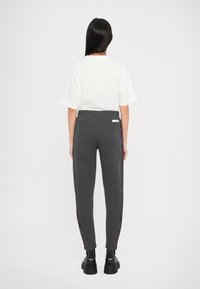 Pantaloni jogger grigi con un design aderente, vita elastica e strisce laterali a motivo geometrico. Abbinate a una t-shirt bianca semplice e stivali neri.