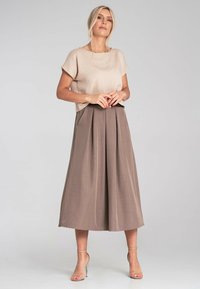 Beżowy top z krótkim rękawem o teksturowanym wykończeniu, zestawiony z brązową plisowaną spódnicą midi, z czarnym paskiem w talii i eleganckimi, cienkimi szpilkami.