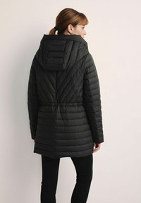 Czarna kurtka puchowa z teksturowanym, pikowanym wzorem, regulowanym elastycznym paskiem w talii i dużym kapturem, widok z tyłu.