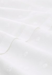 Weißer Stoff mit einer sanften Textur, der ein diskretes Punktmuster aufweist, das gleichmäßig über die Oberfläche verteilt ist und so Tiefe und visuelles Interesse erzeugt.