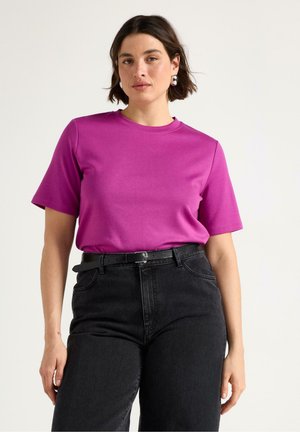 Fuchsia bomulls-t-shirt med korta ärmar och rund halsringning, kombinerad med högmidjade svarta jeans och ett svart bälte.