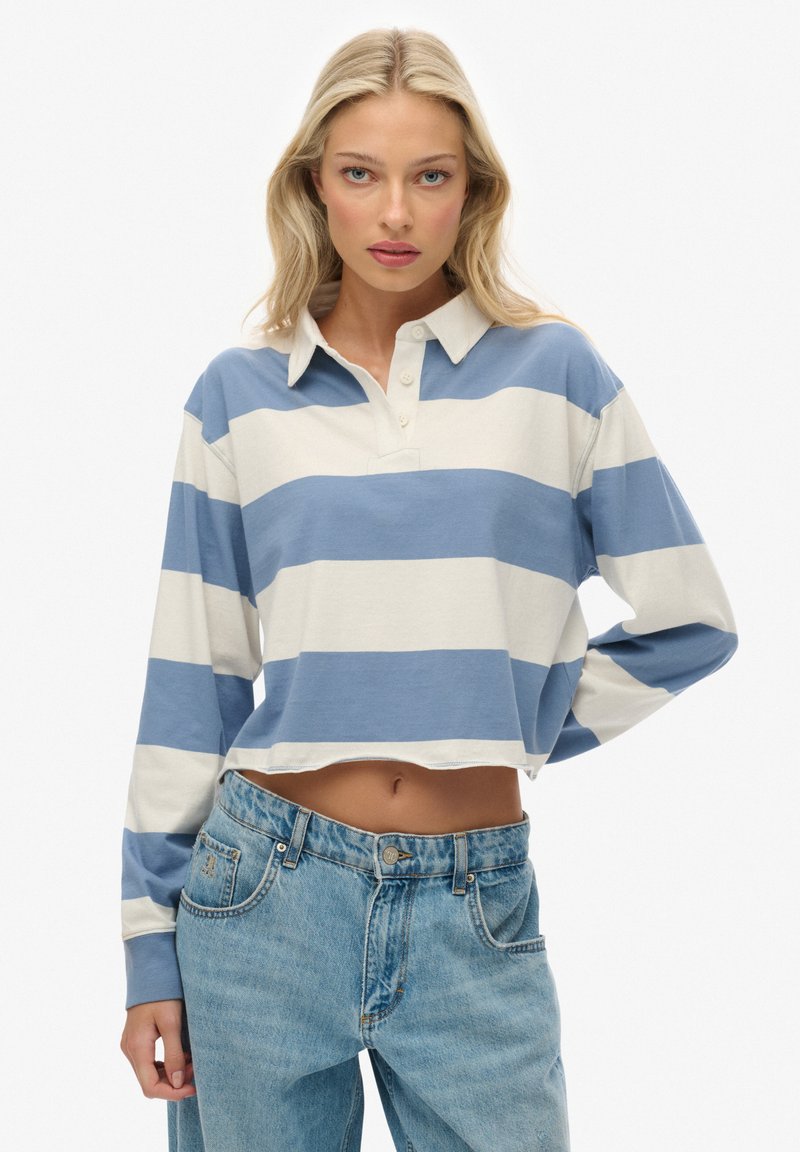 Polo à manches longues recadré à rayures bleu clair et crème, avec un col à revers et trois boutons, associé à un jean en denim taille haute.