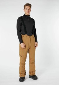 Bruine waterdichte sneeuwbroek met verstelbare zwarte bretels, gecombineerd met een aansluitend zwart longsleeve shirt, gedragen met zwarte laarzen.