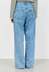 Helle blaue, hoch taillierte, weit geschnittene Jeans mit einer verwaschenen Textur, zwei Gesäßtaschen und einem Logodetail über der rechten Tasche.