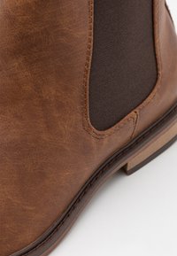 Bottine marron avec une tige en simili cuir texturé, des panneaux latéraux élastiques et un solide talon avec des détails cousus.