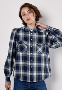 Blue and white plaid long-sleeve shirt with button front, two chest pockets, and shoulder detailing. Cotton fabric, relaxed fit.