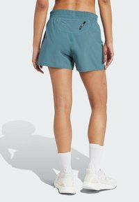 Türkise Sportshorts mit elastischem Bund, ausgestattet mit Seitentaschen und schwarzen Streifen an den Seiten. Weicher, glatter Stoff.