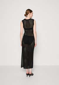 Rochie neagră din plasă transparentă, cu un design fără mâneci, având o croială lungă și fante adânci, asortată cu pantaloni scurți negri. Textură netedă.