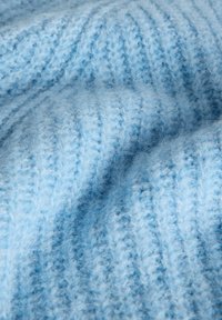 Gaiši zils adīts audums ar mīkstu, pūkainu tekstūru. Raksturīgas ribotas līnijas un dažādas zilo nokrāsu variācijas, kas dizainam piešķir dziļumu.