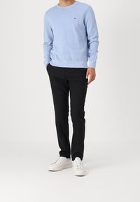 Pull tricoté bleu clair avec encolure ronde, associé à un pantalon slim noir et des baskets blanches. Présente un marquage minimaliste sur la poitrine.