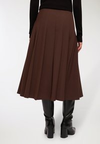 Gonna midi plissettata marrone con una texture liscia, caratterizzata da una cintura ampia e abbinata a stivali neri al ginocchio.