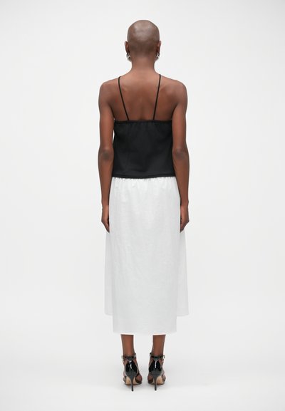 Top à bretelles noires avec corsage ajusté, associé à une jupe blanche longue jusqu'à la cheville. Des chaussures à talons hauts noires complètent le look.