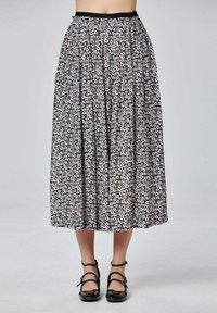 Jupe midi à motif floral avec plis, portée avec des talons à trois bandes en vernis noir, montrée de la taille aux pieds sur un arrière-plan neutre.