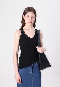 Svart ribbad tanktop med v-hals og blondekant. Kombinert med et dongeri skjørt og en svart skinn skulderveske.