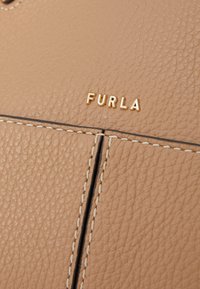 Bež torba od kože s teksturiranom površinom, kontrastnim šavovima i zlatnim embossed "Furla" logom na površini.