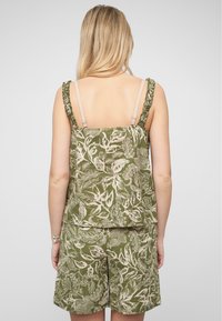 Olivovo zelený dvojdielny outfit, ktorý obsahuje top bez rukávov s volánovými ramienkami a šortky, obidva zdobené krémovým botanickým vzorom.