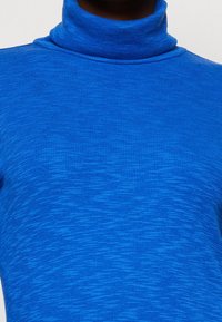 Maglione blu a collo alto con coste, caratterizzato da un tessuto a maglia testurizzato, dalla forma aderente e da un motivo leggermente più chiaro di blu su tutta la superficie.