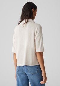 Kortärmad, ljus beige tröja med strukturerad stickning, med krage, något kortad design och avslappnad passform, i kombination med blå jeans.