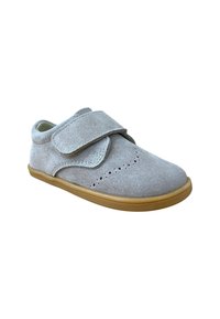 Zapato infantil de ante gris claro con detalles perforados y una amplia correa de Velcro, con una suela de goma marrón.