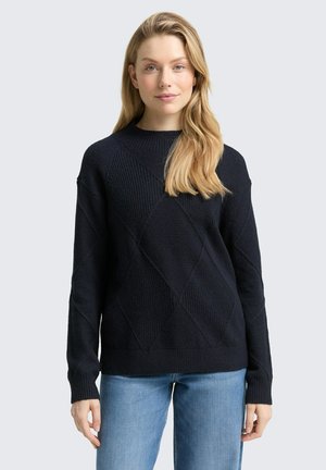 Pull en maille bleu marine avec un motif en losange, col rond et poignets côtelés. Associé à un jean bleu clair. Un design texturé et décontracté.