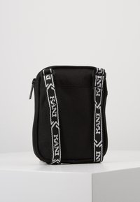 Borsa in tessuto nero con chiusura a zip, caratterizzata da due manici bianchi a contrasto e un logo del marchio. Texture liscia, forma rettangolare compatta.