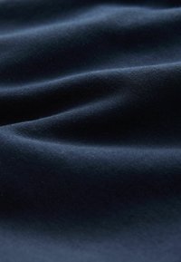 Marineblaue Stoff mit glatter Textur, der sanfte Falten aufweist. Das Material wirkt leicht und leicht reflektierend. Keine sichtbaren Muster oder Designs.