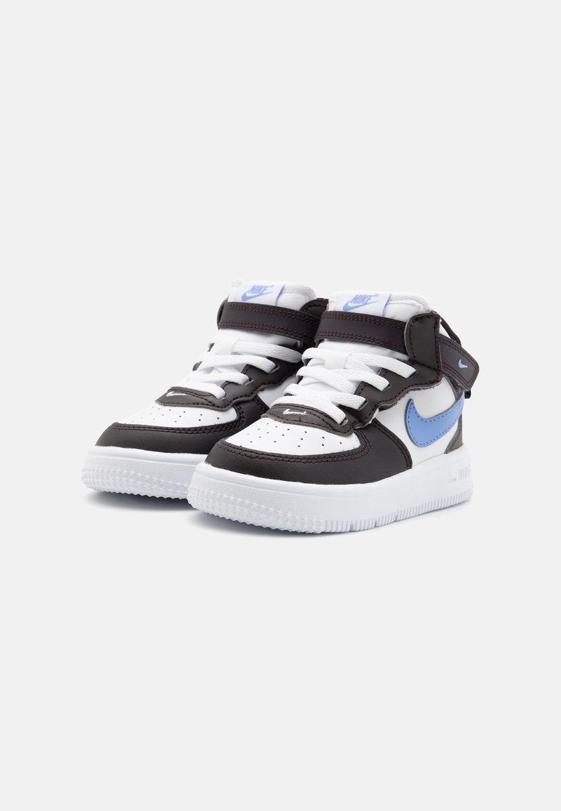 Baskets Nike Air Force 1 blanches et marron avec des accents bleus, en cuir, comprenant une boîte à orteils perforée et une sangle ajustable en Velcro.