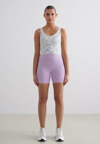 Floral tank top with a v-neckline in light pastel colors, paired with solid lavender bike shorts. White athletic shoes complete the look.