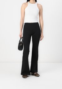 Bílý žebrovaný top s halter krkem, černé zvonové kalhoty, černá kabelka a hnědé baleríny s leopardím vzorem. Minimalistický design s čistými liniemi.