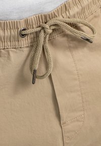 Pantalones cortos beig con una cinturilla ajustable, que presentan una textura tejida y acentos metálicos. Incluyen un bolsillo lateral.