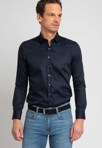 Marineblauw shirt met lange mouwen in een gladde stof met een aansluitend ontwerp, voorzien van een puntige kraag en knopen aan de voorkant. Gecombineerd met lichtblauwe spijkerbroeken.