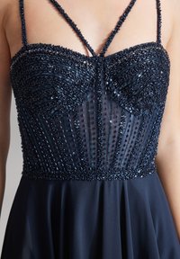 Abito blu navy con un bustier decorato da perline e modelli intricati, dettagli in rete e spalline sottili che conducono a una gonna fluente.