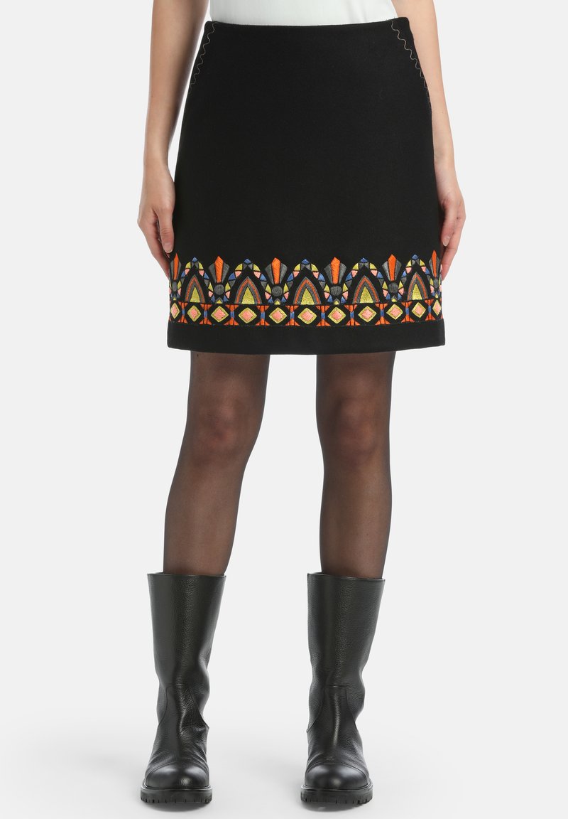 Crna vuna suknja s šarenim vezenim geometrijskim uzorcima duž rubova. Tekstura tkanine i kontrastni detalji šivanja.