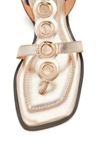 Sandal de color dorado metálico con tres acentos circulares metálicos en la correa, textura suave, forma de punta afilada y suela plana negra.