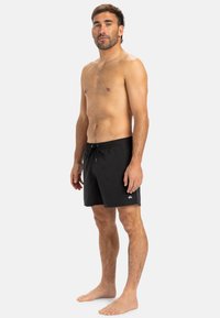 Schwarze Badeshorts mit elastischem Bund und Kordelzug. Hergestellt aus leichtem Material mit einem kleinen Logo auf der unteren linken Seite.