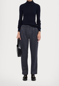 Navy turtleneck neulepaita yhdistettynä harmaisiin joustovyötäröisiin housuihin, joissa on hienovarainen tekstuuri. Musta laukku ja loaferit täydentävät asun.