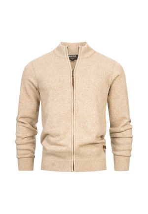 Pull zippé beige avec un col montant, des poignets et un ourlet côtelés. Texture en tricot douce avec une petite étiquette de marque sur le côté inférieur.