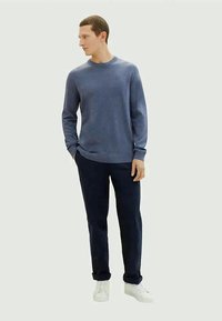 Pulôver azul texturizado com gola redonda, emparelhado com calças escuras azuis-marinho e ténis brancos. Conjunto casual simples e clássico.