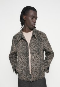 Giacca con stampa leopardata con chiusura frontale a zip, colletto e tasche lungo le cuciture laterali. Realizzata in tessuto testurizzato nei toni del marrone e nero.