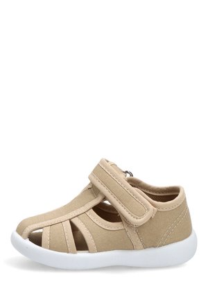 Sandalia beige para niño pequeño con tira de velcro, talón cerrado, punta abierta y suela blanca flexible.