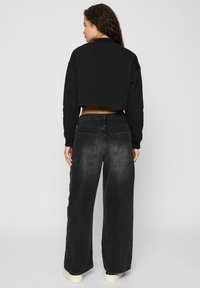 Svart crop sweatshirt med høy hals, kombinert med løstsittende svarte jeans som har en falmet tekstur og to baklommer.