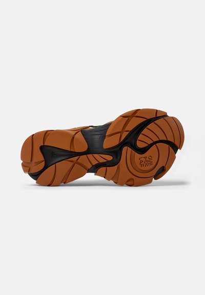 Suola di sneaker nera e marrone con una trama ondulata, caratterizzata da battistrada pronunciate e un dettaglio logo circolare sul tallone.