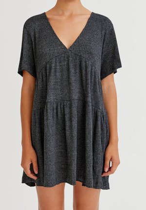 Krótka ciemnoszara prążkowana sukienka z krótkimi rękawami i dekoltem w serek, noszona przez osobę widoczną od szyi do połowy ud, stojącą na jednolitym tle.