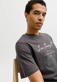 Grå bomulds t-shirt med korte ærmer, med tekstdesign foran og en afslappet pasform, præsenteret på en model foran en hvid baggrund.