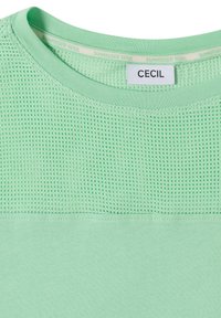 Chemise vert menthe avec col rond, panneau supérieur en maille au niveau de la poitrine, et étiquette blanche indiquant "CECIL" à l'intérieur du col.