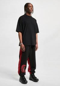 Black oversized t-shirt, relaxed fit. Black and red sweatpants with tiger graphic on the left leg. Black lace-up boots complement the outfit.